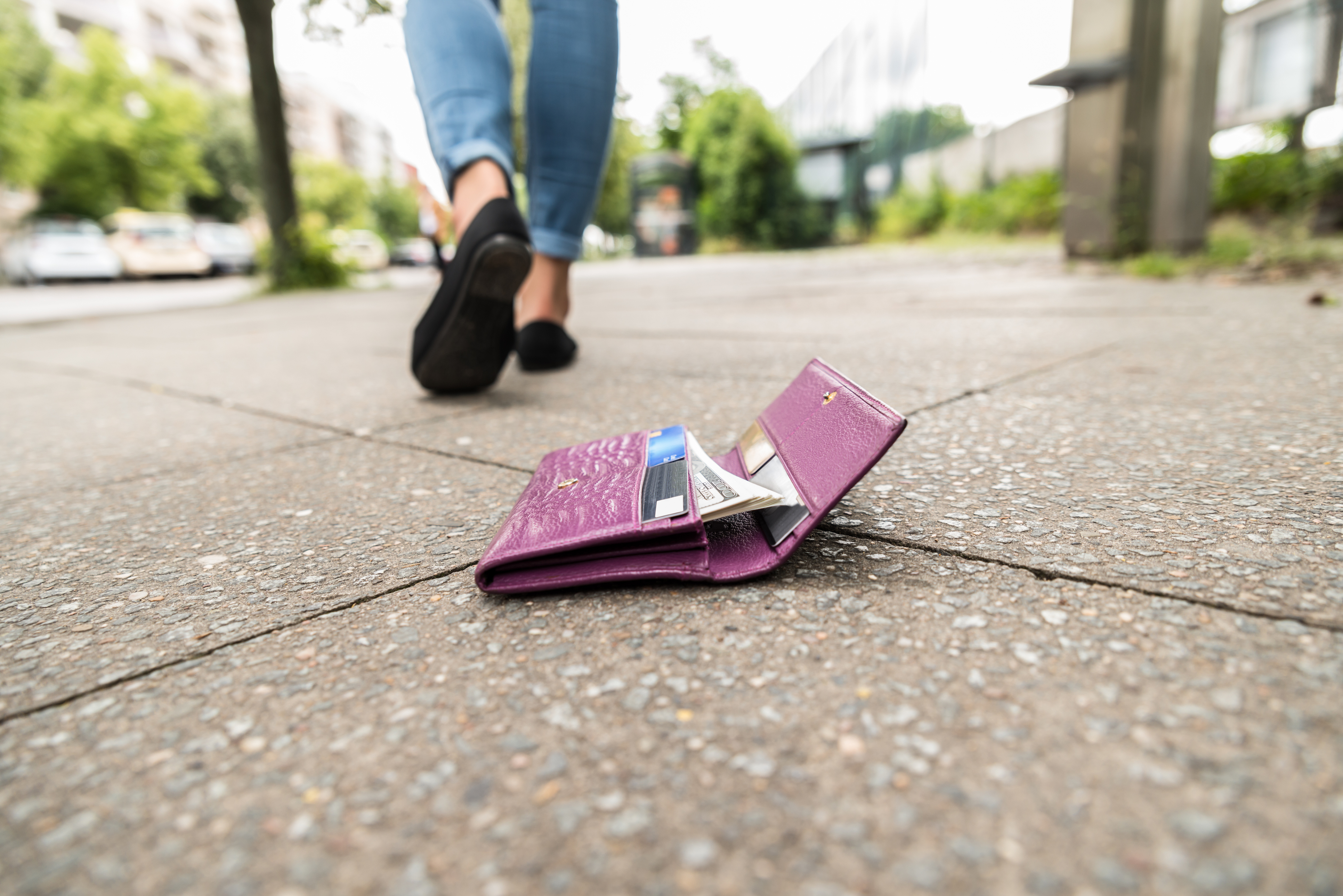 woman walking away from dropped wallet on ground 
