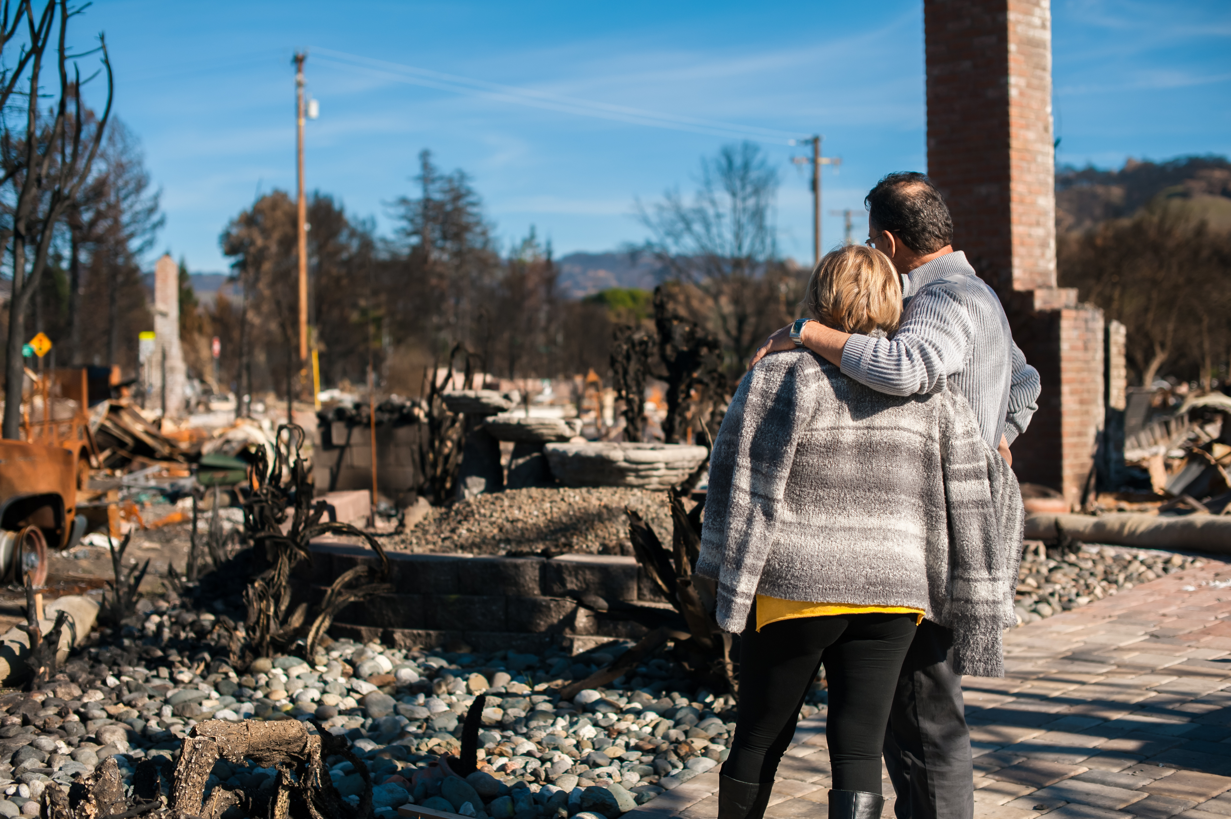 older couple standing in front of natural disaster damage/remains