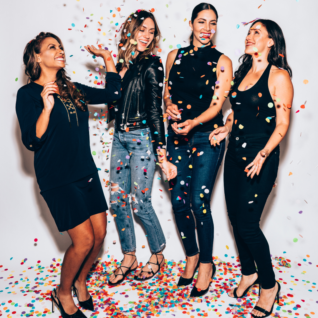 4 women standing and smiling with confetti around them