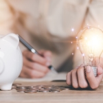 white piggy bank - hand holding lit up light bulb