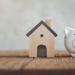 white piggy bank with small wooden house next to it on table
