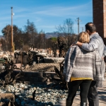 older couple standing in front of natural disaster damage/remains